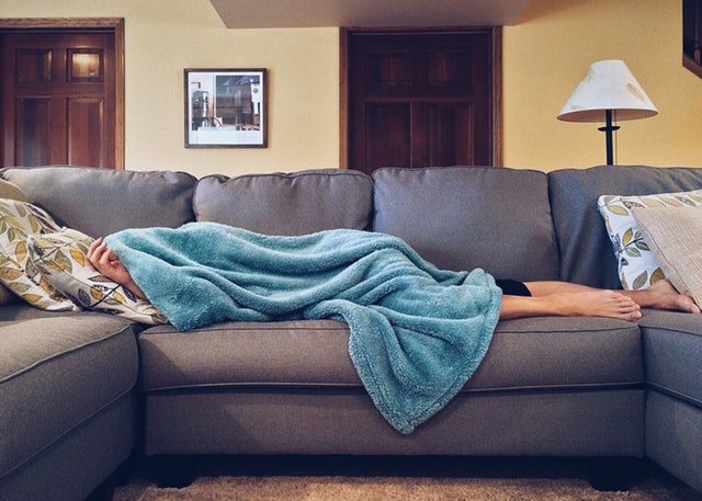 Muž spí na gauči zakrytý s dekou.jpg